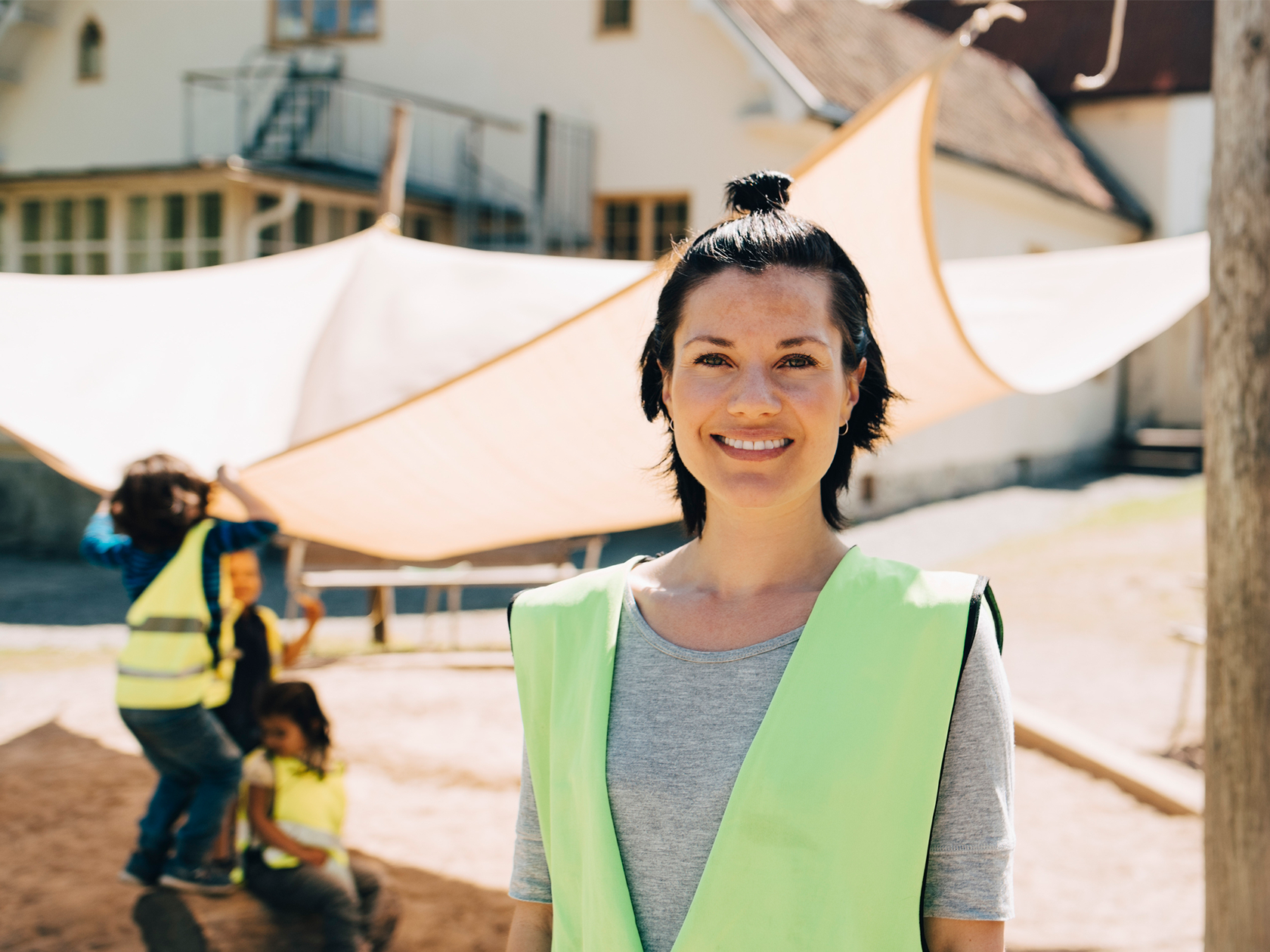 Lärare som ler med barn som leker i bakgrunden