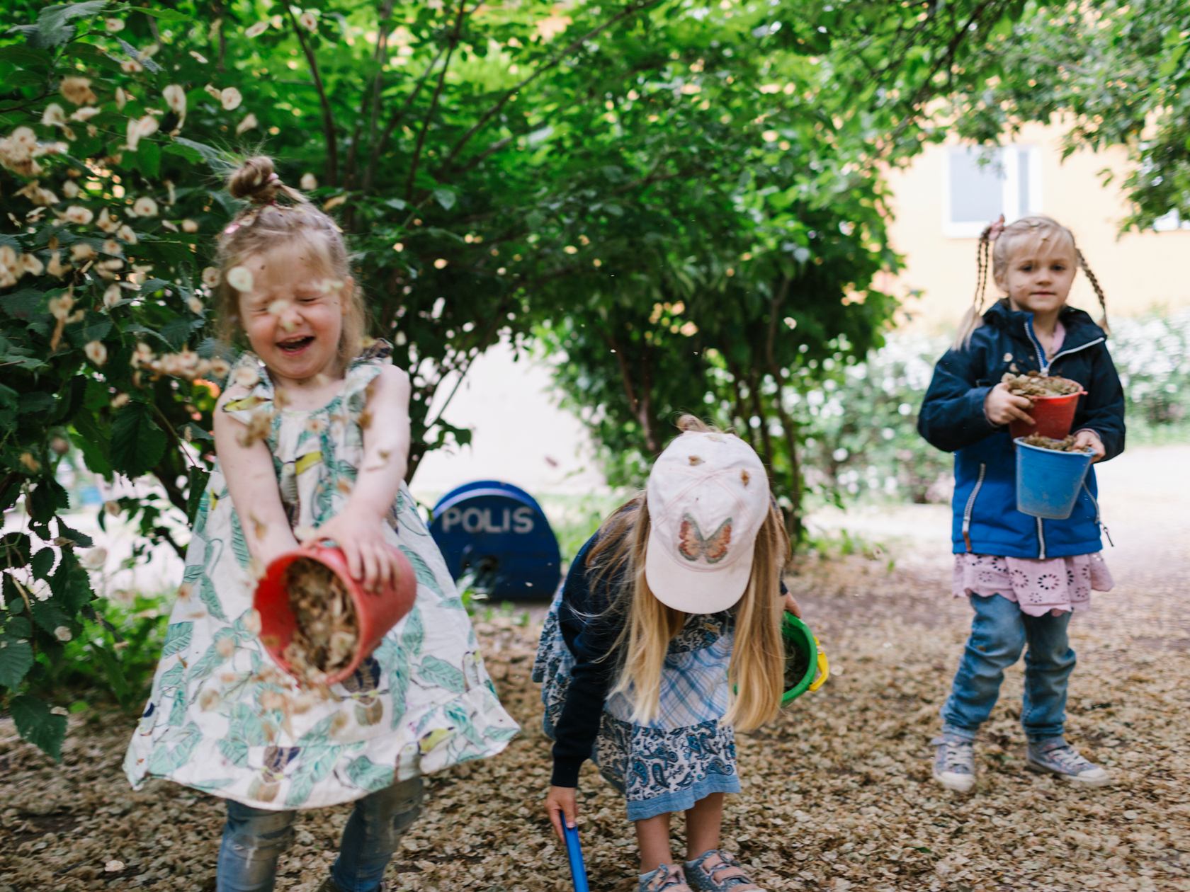 3 förskolebarn som leker med hinkar och blad