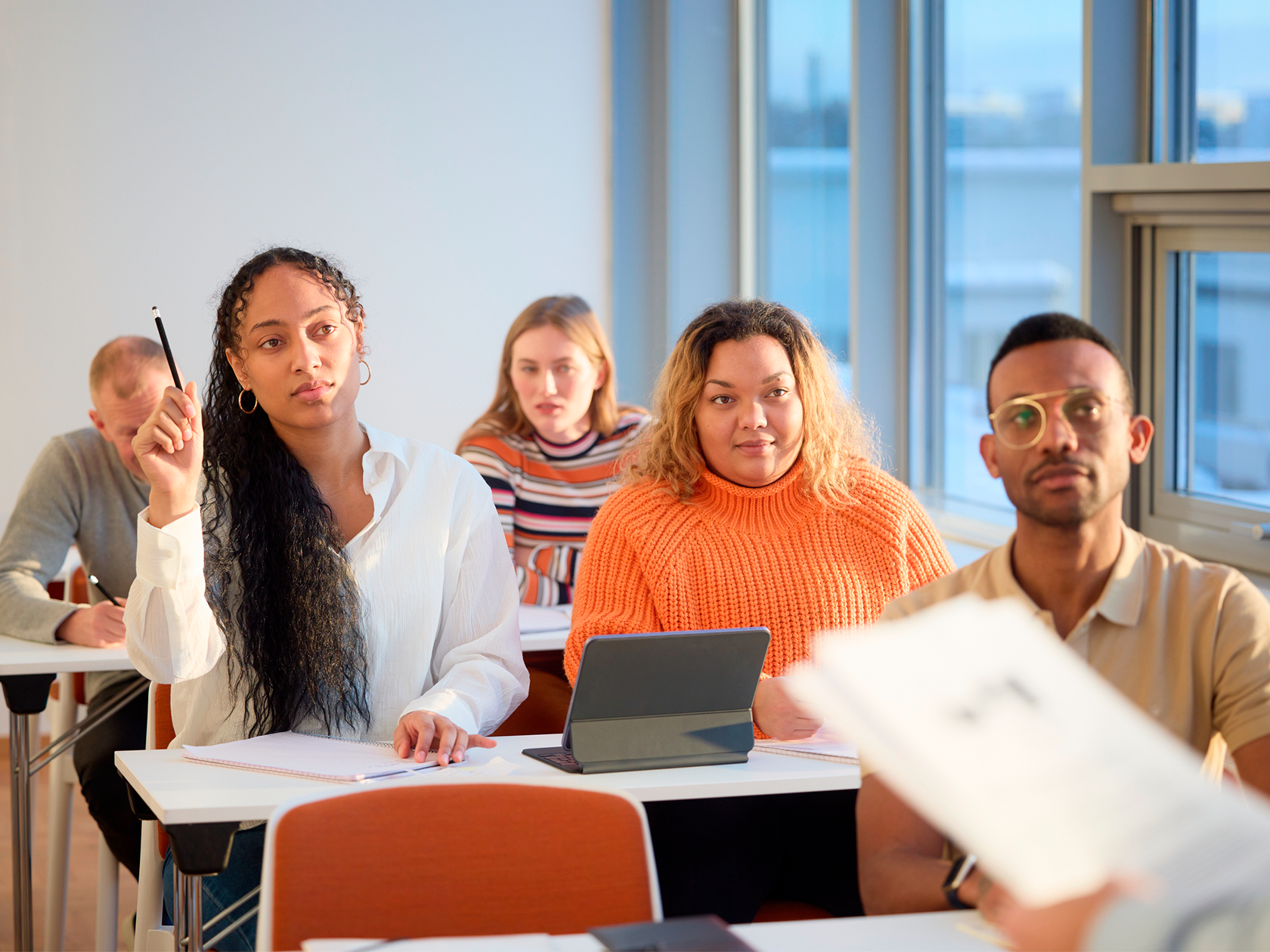 Vuxen elev som räcker upp pennan i ett klassrum med andra elever